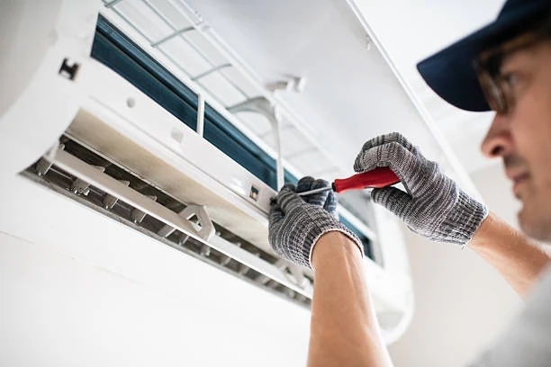 Gloved technician working on an indoor air conditioner with a screwdriver