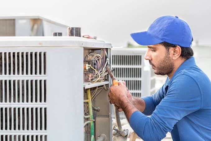 HVAC technician checking electrical connections inside an outdoor condenser