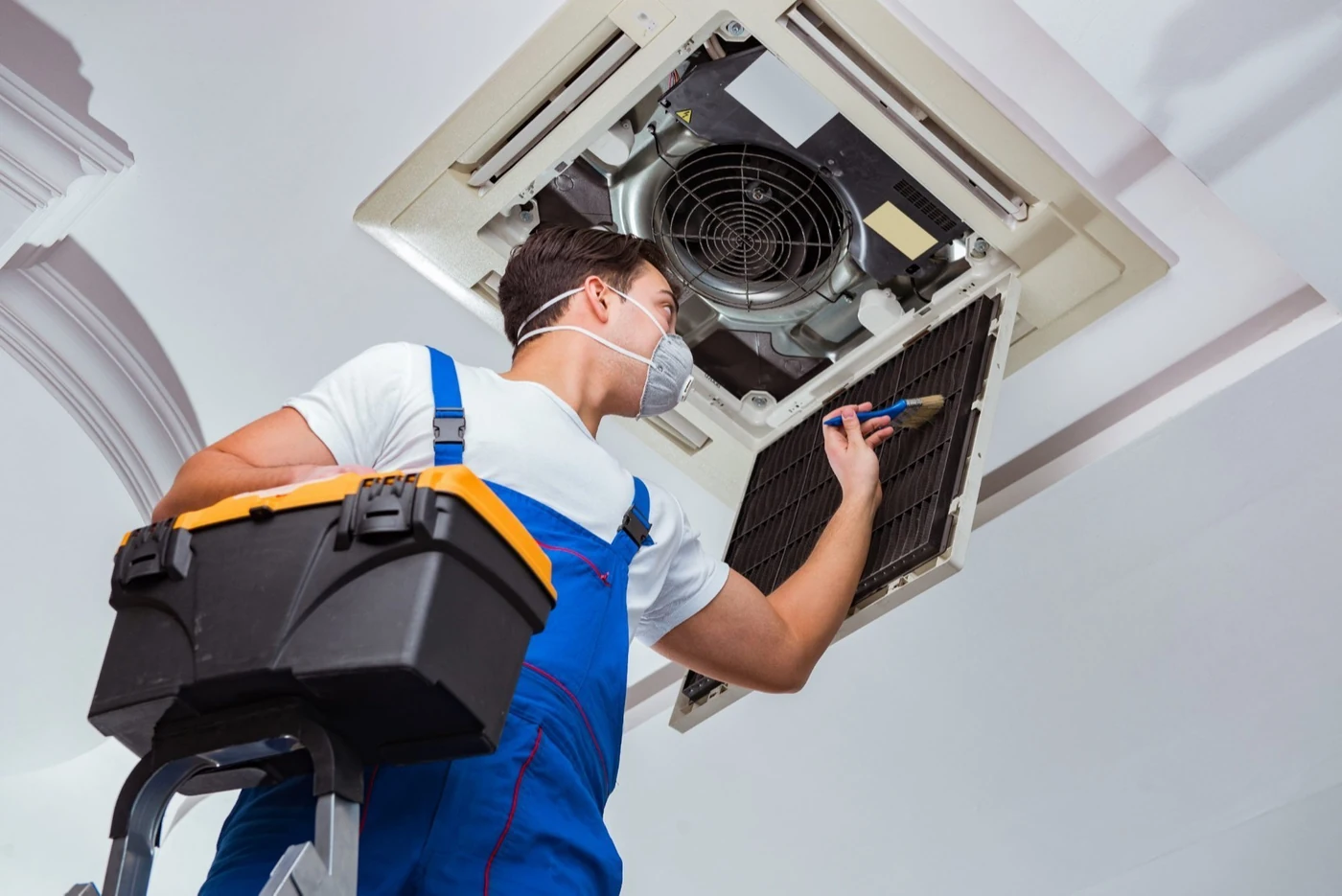 Technician inspecting and cleaning an open ceiling-mounted air conditioning unit